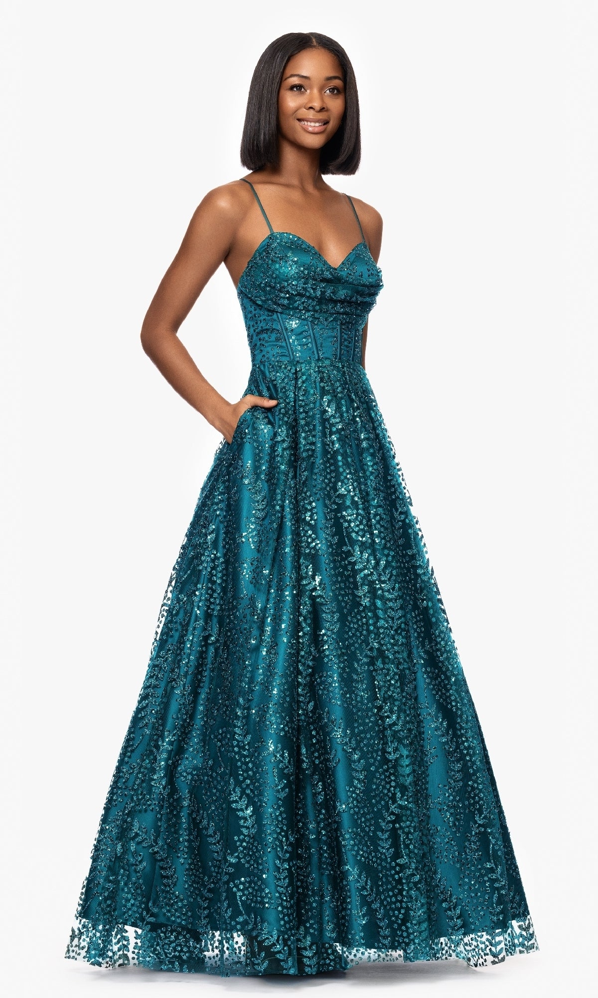 A woman poses against a white background in the Long Glitter Prom Dress: Blondie Nites 4617BN—a teal, floor-length A-line gown featuring sequin details, thin straps, a corset-style bodice, and convenient pockets.
